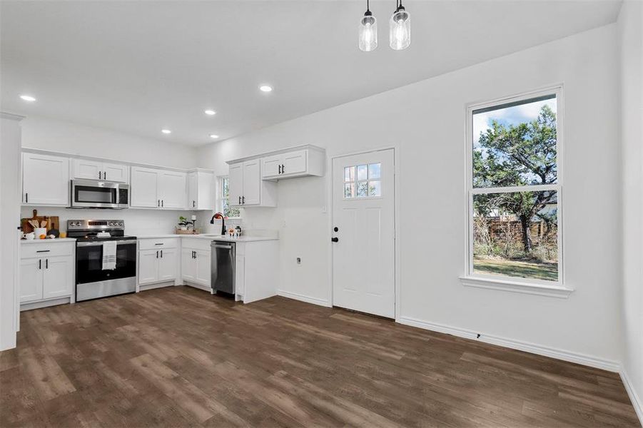 Kitchen with appliances with stainless steel finishes, white cabinets, decorative light fixtures, and plenty of natural light