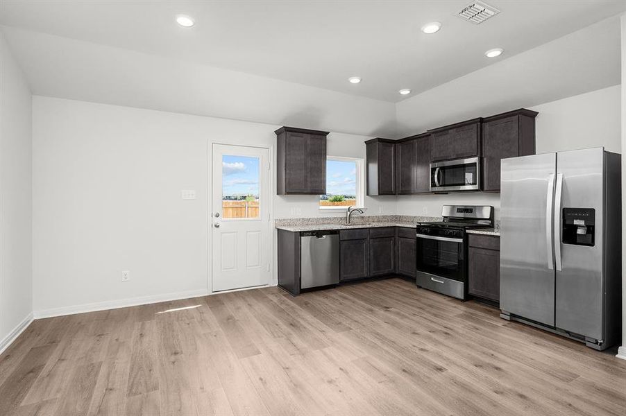 Kitchen featuring stainless steel appliances, recessed lighting, light wood finished floors, dark brown cabinetry, and light stone counters Kitchen featuring stainless steel appliances, recessed lighting, light wood finished floors, dark brown cabinetry, and light stone counters