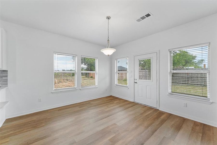 Spacious dining area featuring wood-finish flooring, multiple windows with blinds, a ceiling-mounted light fixture, and a glass-paneled exterior door