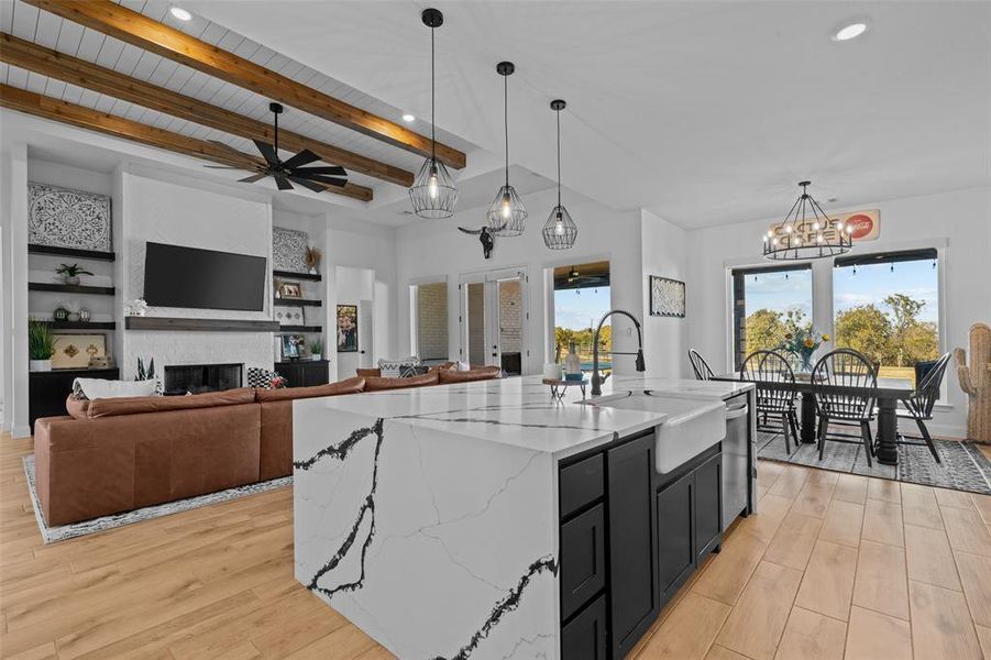 Kitchen with a kitchen island with sink, stainless steel dishwasher, light stone countertops, decorative light fixtures, and light hardwood / wood-style floors