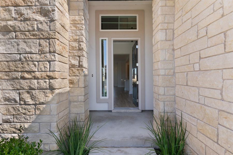 Stone facade entrance beckons guests inside, framed by lush greenery.