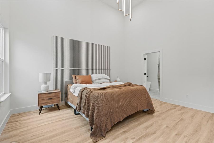 Bedroom with a towering ceiling, light wood-style flooring, baseboards, and multiple windows Bedroom with a towering ceiling, light wood-style flooring, baseboards, and multiple windows