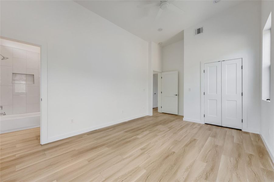 Unfurnished bedroom featuring light wood-style floors, ceiling fan, a towering ceiling, and a closet Unfurnished bedroom featuring light wood-style floors, ceiling fan, a towering ceiling, and a closet