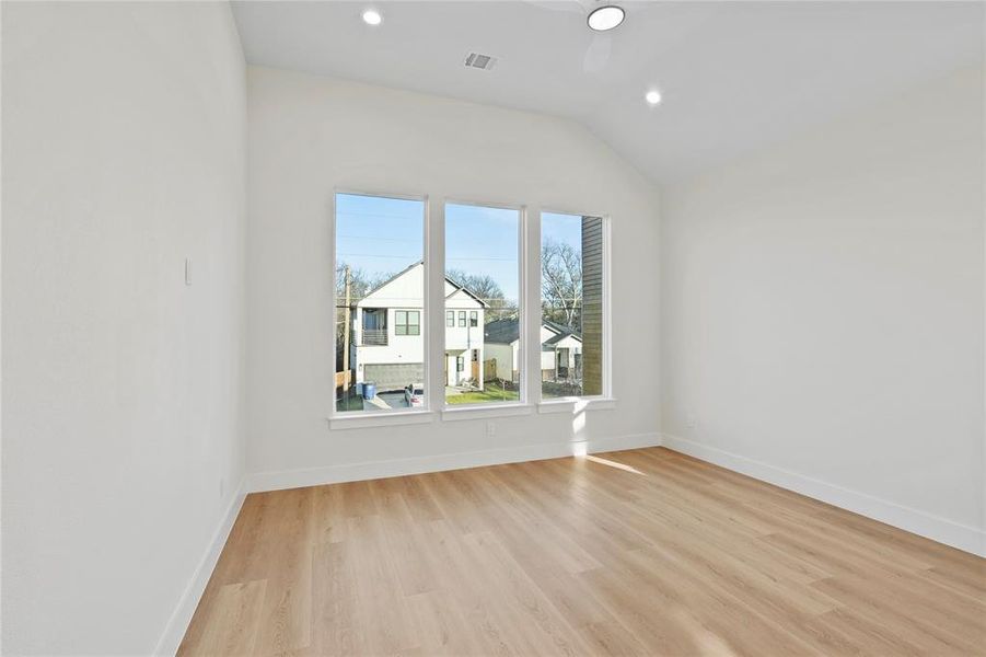 Empty room with baseboards, vaulted ceiling, visible vents, and light wood-style floors