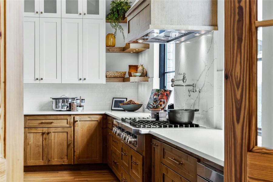 Kitchen featuring custom exhaust hood, white cabinets, and backsplash