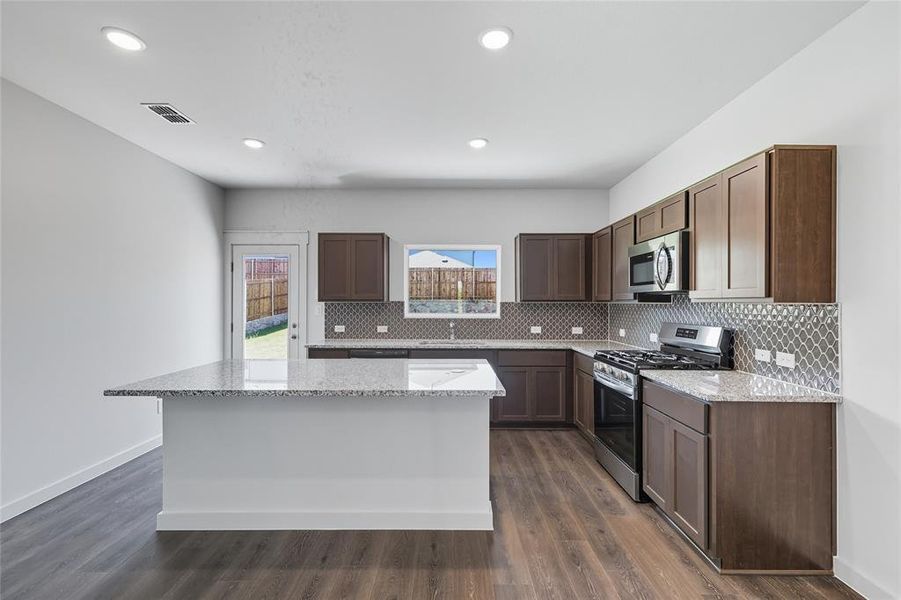 Kitchen featuring stainless steel appliances, decorative backsplash, light stone countertops, dark wood finished floors, and recessed lighting Kitchen featuring stainless steel appliances, decorative backsplash, light stone countertops, dark wood finished floors, and recessed lighting