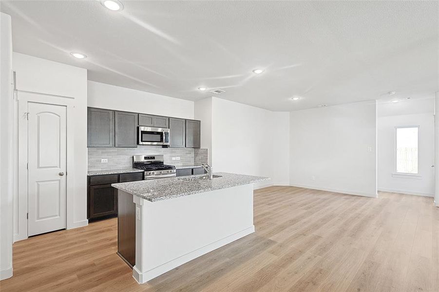 Kitchen featuring appliances with stainless steel finishes, light hardwood / wood-style floors, and an island with sink