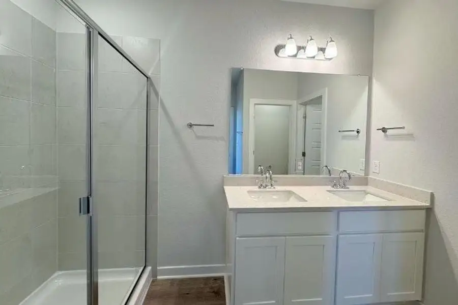 Bathroom featuring a shower stall, double vanity, and wood finished floors
