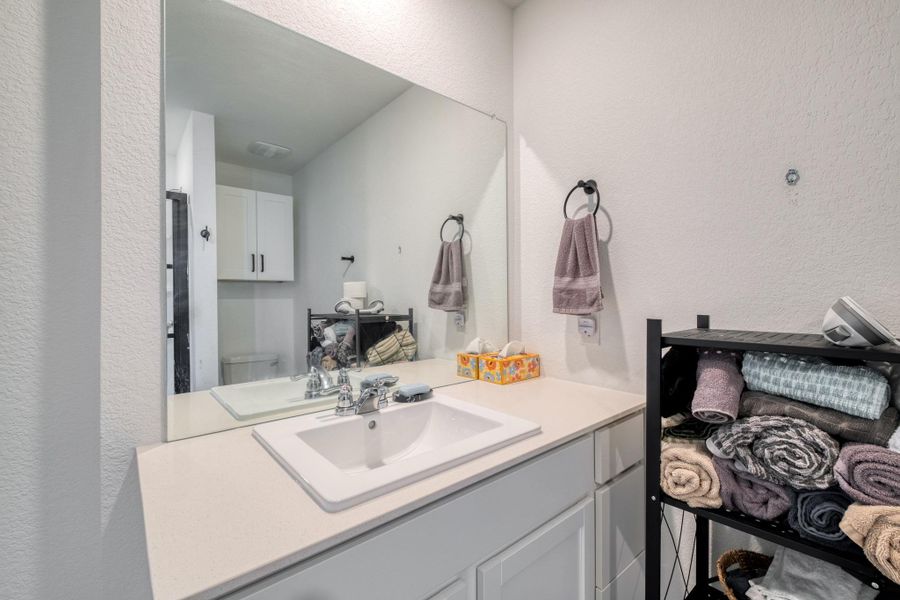 Bathroom featuring a spacious vanity with a white countertop and an integrated sink, a large wall-mounted mirror, and cabinet storage below