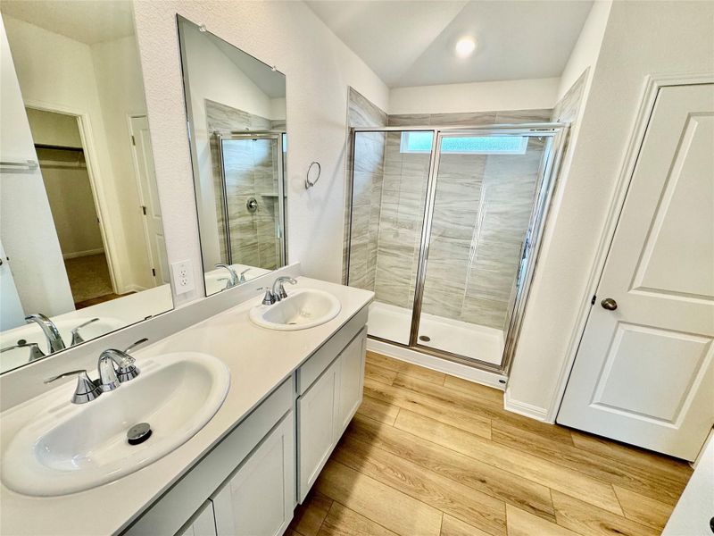 Full bathroom featuring a stall shower, light wood finished floors, double vanity, a spacious closet, and vaulted ceiling