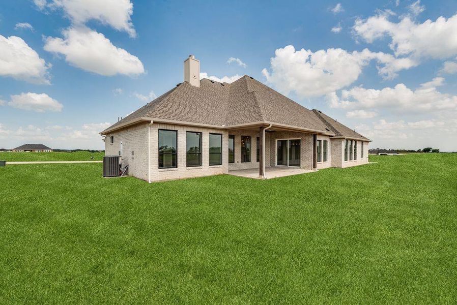 Rear view of property with brick siding, a lawn, a patio area, and a shingled roof
