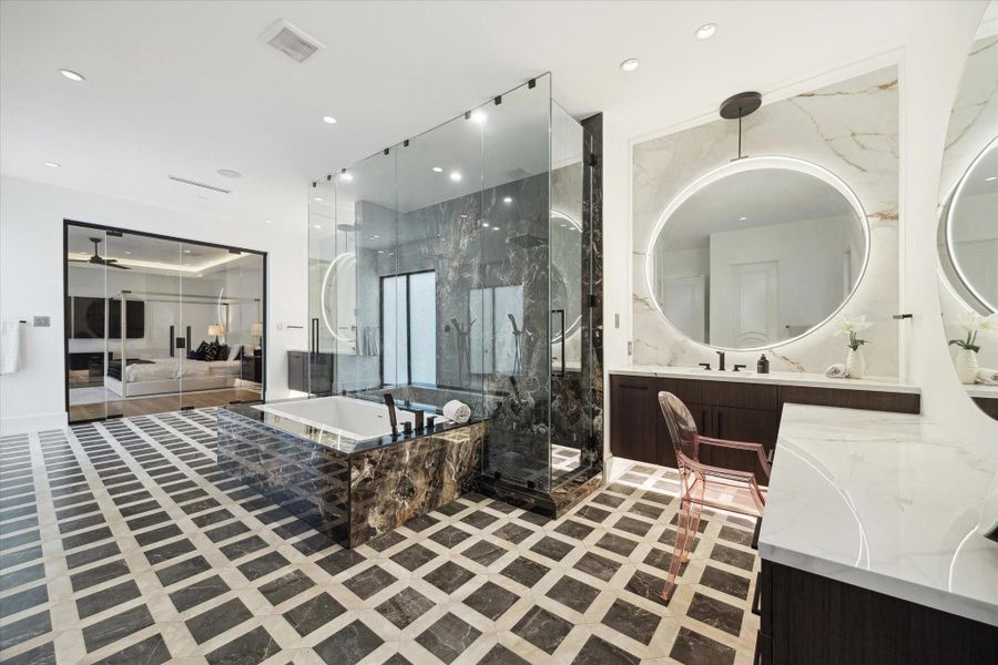 Through a custom designed framed glass door, escape to this spa-like lavish primary bathroom with dual his/hers vanities & elegant LED mirrors, Two water closets and luxury patterned tile floors.