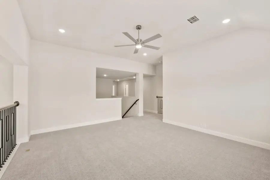 Open upstairs loft with gray carpet, ceiling fan, and staircase railing opening