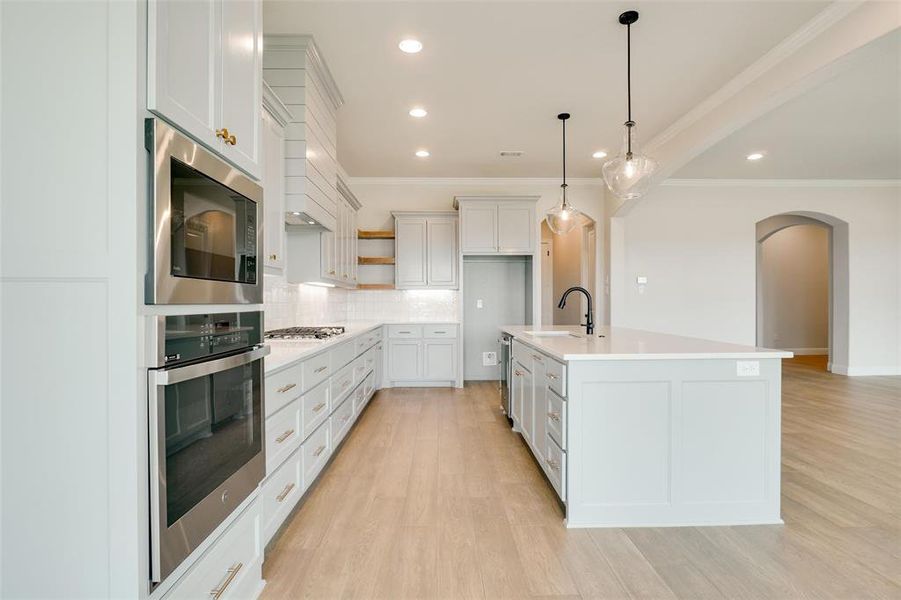 Kitchen featuring light hardwood / wood-style flooring, stainless steel microwave, backsplash, and a kitchen island with sink