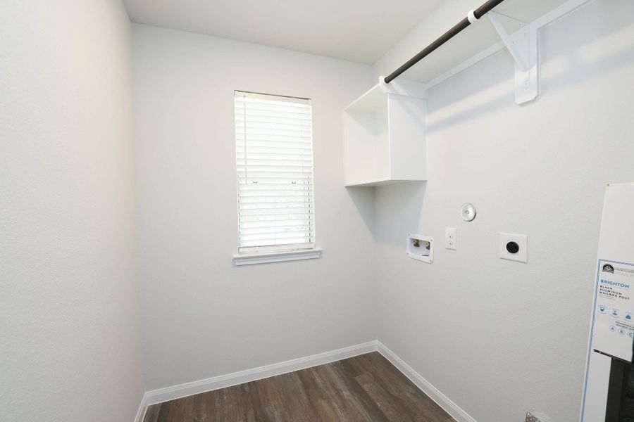 This photo showcases a compact, well-lit laundry room with a window, hookups for a washer and dryer, and a shelf with a hanging rod for storage.
