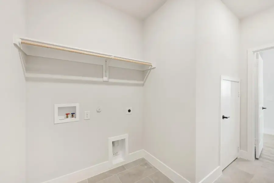 Laundry room with wall-mounted shelf, clothes rod, washer hookups, and dryer vent on tile floor