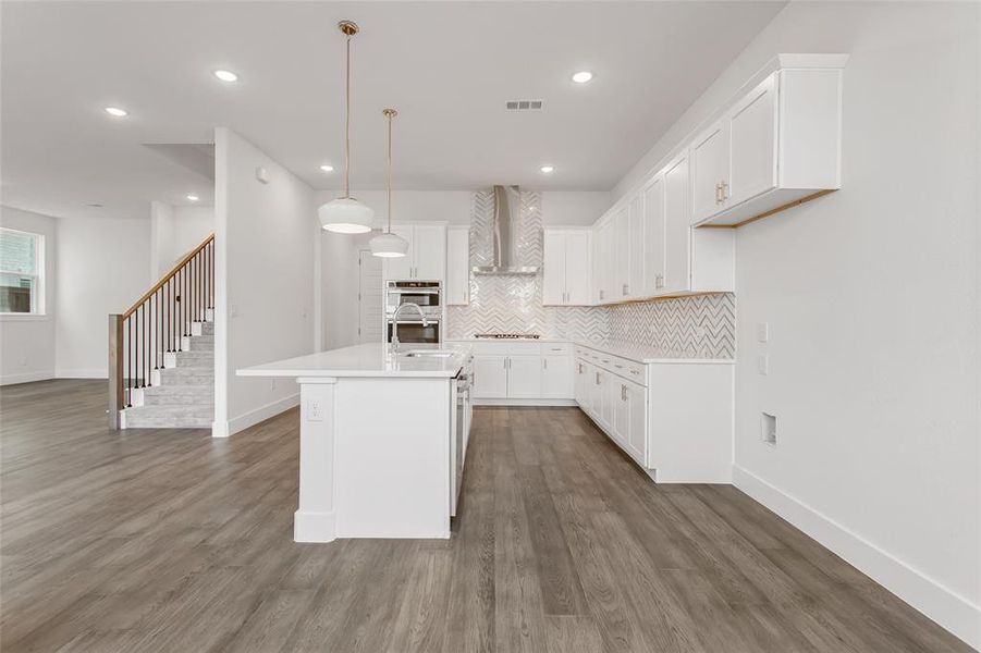 Kitchen featuring white cabinets, wall chimney range hood, sink, an island with sink, and stovetop