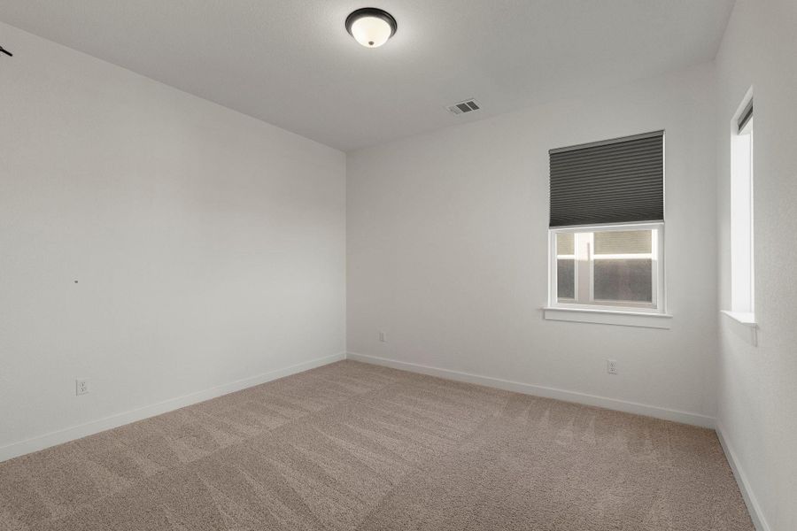 A spacious, naturally illuminated room featuring plush carpeting and a bright overhead light fixture.