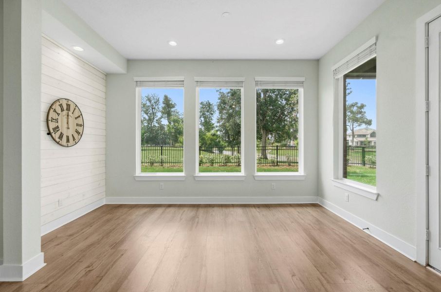 The Breakfast Room is a bright and inviting space, beautifully framed by a quartet of picture windows that showcase peaceful, tree-filled Backyard views and fill the room with natural light. A charming shiplap accent wall echoes the design of the Kitchen island, creating a cohesive and thoughtfully curated aesthetic. Completing the space, a sleek glass-plated door provides seamless access to the covered Back Patio, blending indoor comfort with effortless outdoor living and entertaining.