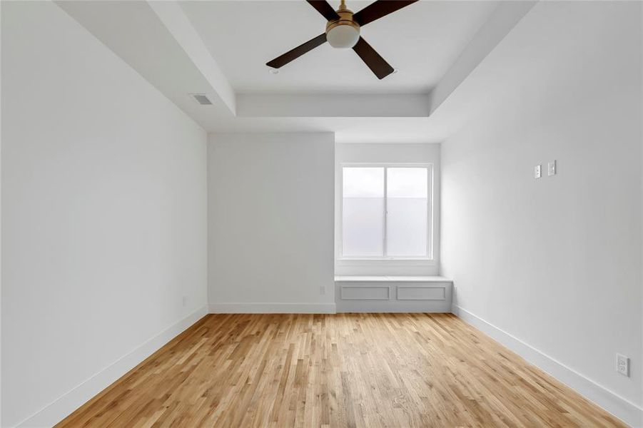 Unfurnished room with a raised ceiling, ceiling fan, and light wood finished floors
