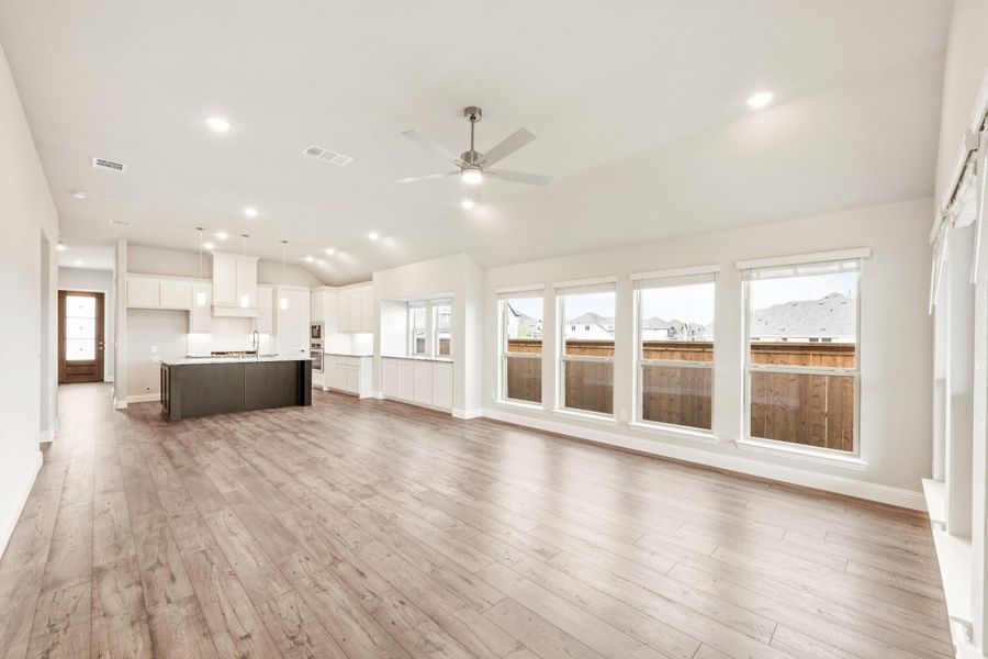 Open-concept living area with hardwood floors, ceiling fan, and kitchen with dark island and white cabinets in background Open-concept living area with hardwood floors, ceiling fan, and kitchen with dark island and white cabinets in background