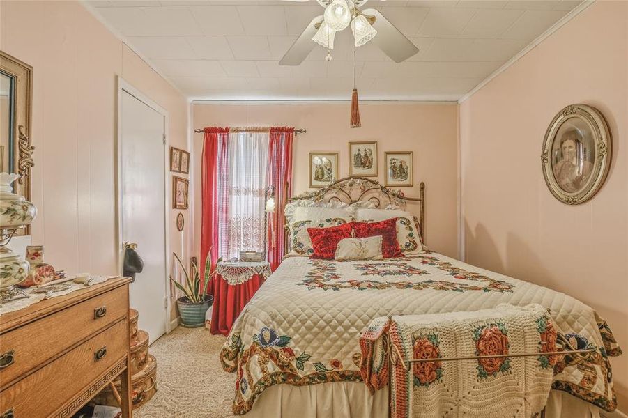 Bedroom featuring a ceiling fan with integrated lighting, wall-to-wall carpeting, and a window with sheer and red drapery Bedroom featuring a ceiling fan with integrated lighting, wall-to-wall carpeting, and a window with sheer and red drapery