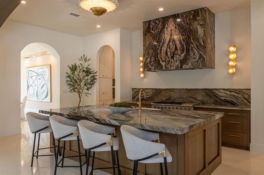 Kitchen with light tile patterned floors, dark stone counters, arched walkways, a kitchen breakfast bar, and recessed lighting