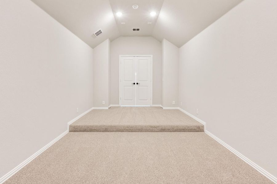 Empty room with vaulted ceiling, beige carpet, raised platform, and white double doors at the end Empty room with vaulted ceiling, beige carpet, raised platform, and white double doors at the end