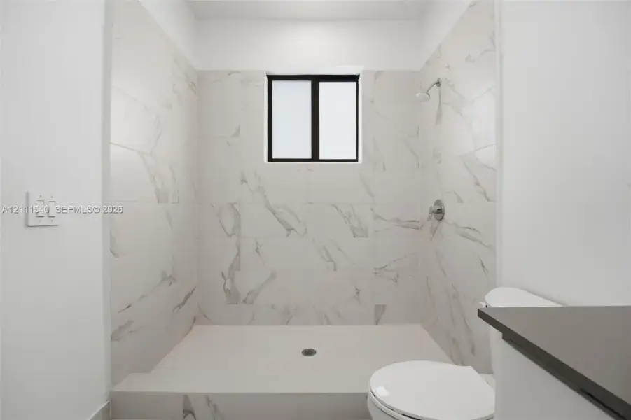 Walk-in shower enclosure featuring large-format stone-patterned tile walls, fixed window, chrome shower fixture, and built-in shower floor
