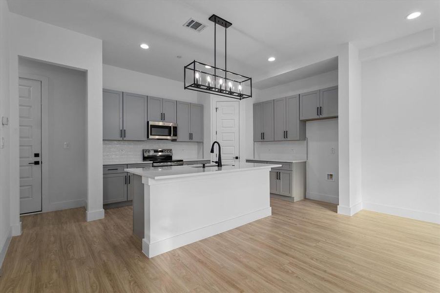 Kitchen with gray cabinets, a center island with sink, tasteful backsplash, appliances with stainless steel finishes, and hanging light fixtures Kitchen with gray cabinets, a center island with sink, tasteful backsplash, appliances with stainless steel finishes, and hanging light fixtures