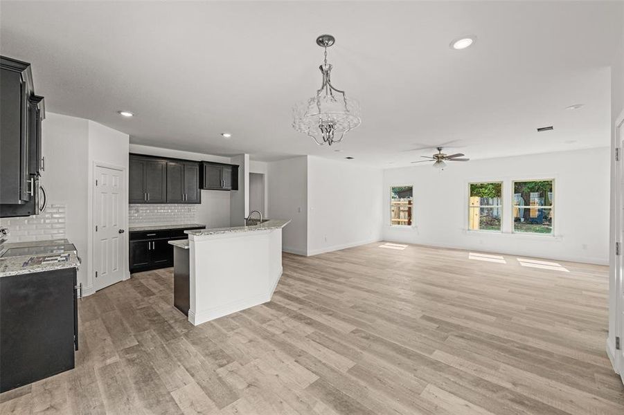 Kitchen with decorative backsplash, ceiling fan with notable chandelier, light hardwood / wood-style floors, and a center island with sink