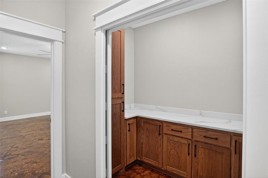 Built-in wood-finish cabinetry featuring black hardware, a white countertop, and a tall pantry cabinet Built-in wood-finish cabinetry featuring black hardware, a white countertop, and a tall pantry cabinet