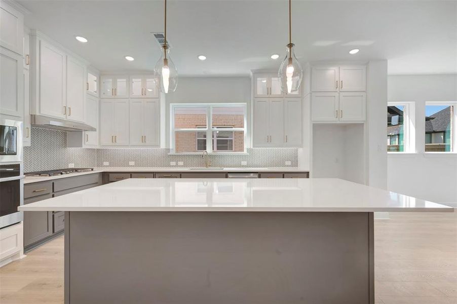 Kitchen with a center island, light wood-type flooring, glass insert cabinets, stainless steel appliances, and dual tone cabinetry
