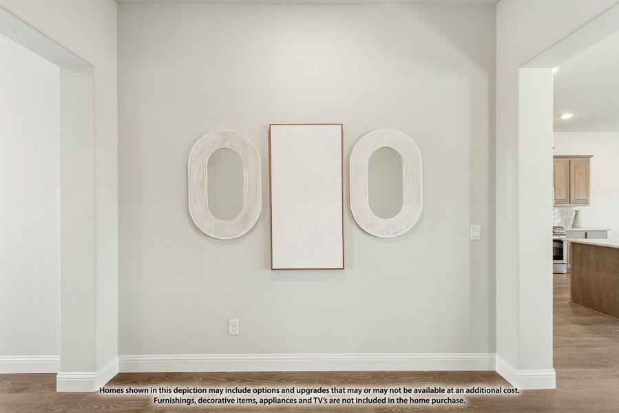 Hallway with white walls, hardwood floors, and three decorative wall art pieces, with kitchen visible in background. Hallway with white walls, hardwood floors, and three decorative wall art pieces, with kitchen visible in background.