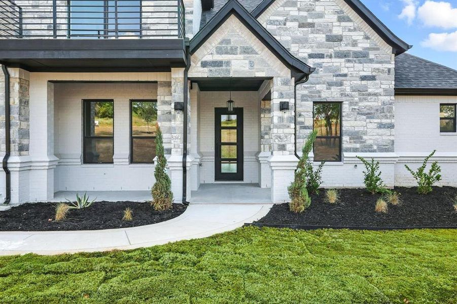 View of exterior entry featuring brick siding, a lawn, and stone siding View of exterior entry featuring brick siding, a lawn, and stone siding