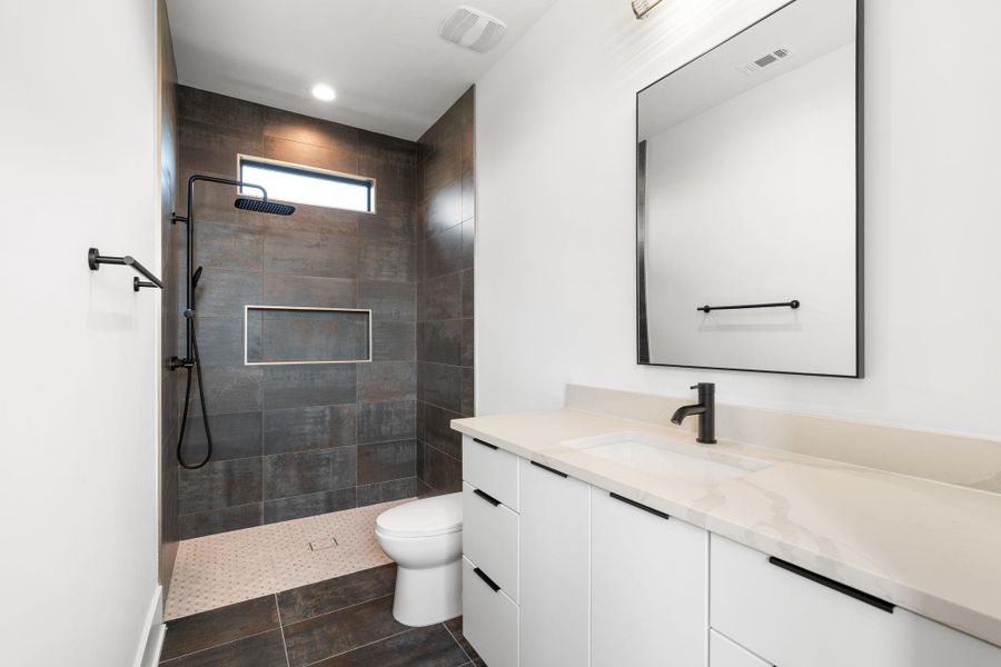 Modern bathroom featuring sleek dark tiled shower with rain head and a spacious vanity with a rectangular sink.