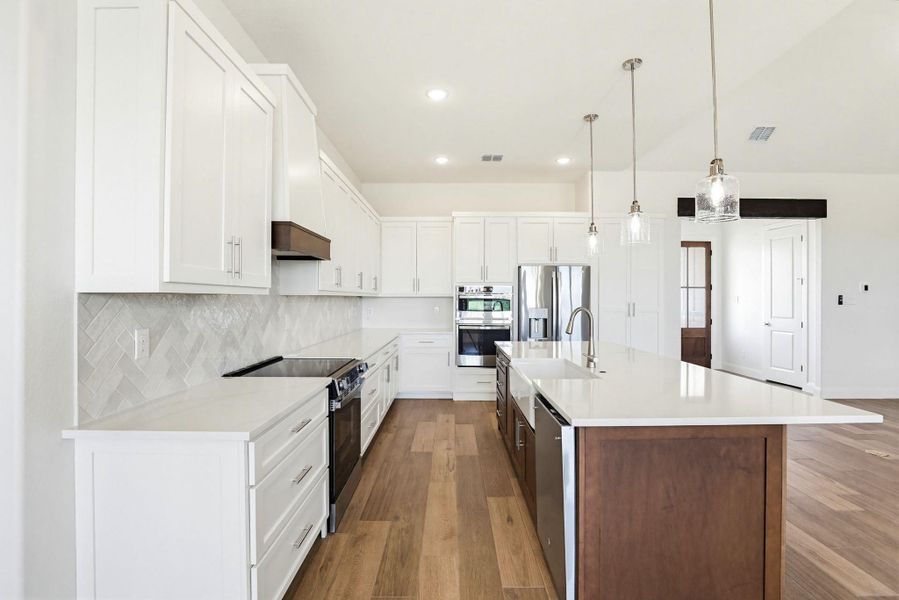 A well-appointed kitchen features a large island and ample white cabinetry, illuminated by modern pendant lights.