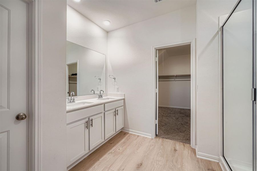 Full bath with a spacious closet, double vanity, light wood-style flooring, and a stall shower