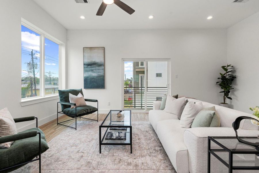 This inviting living area features recessed lighting, a ceiling fan for comfort, and sliding doors that open to a second-story balcony—perfect for indoor-outdoor flow and fresh air.