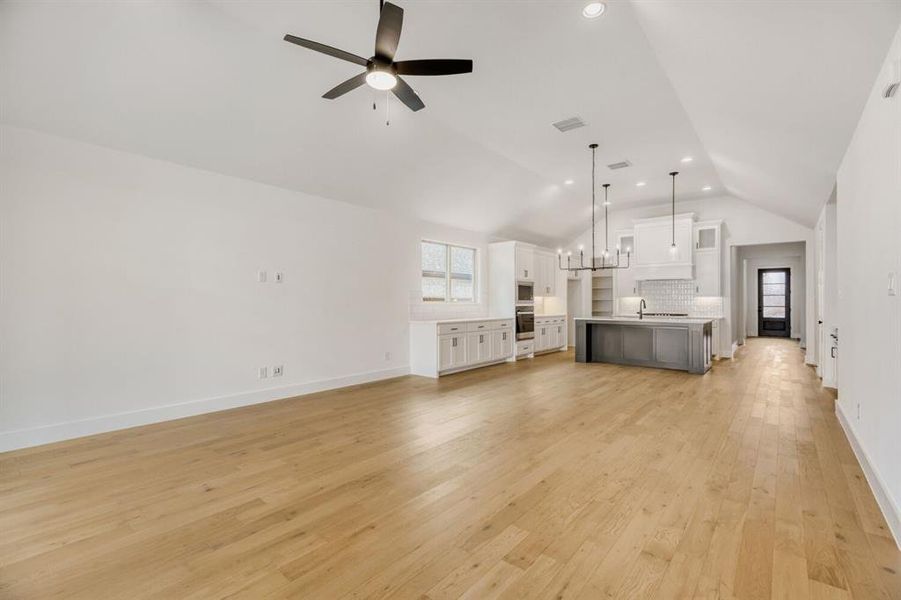 Unfurnished living room with hanging lights, a ceiling fan, light wood finished floors, and lofted ceiling