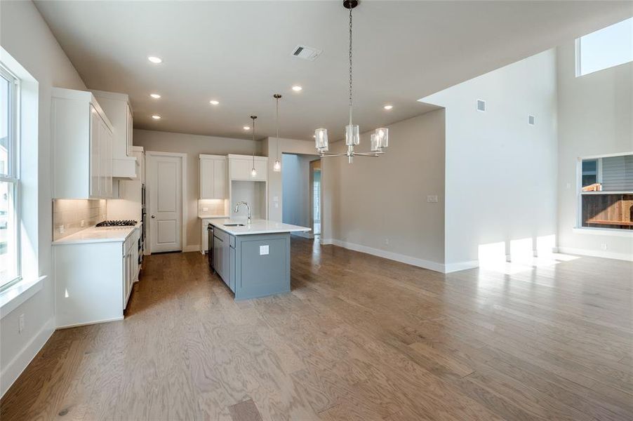 Kitchen with sink, light wood-type flooring, a kitchen island with sink, hanging light fixtures, and white cabinets