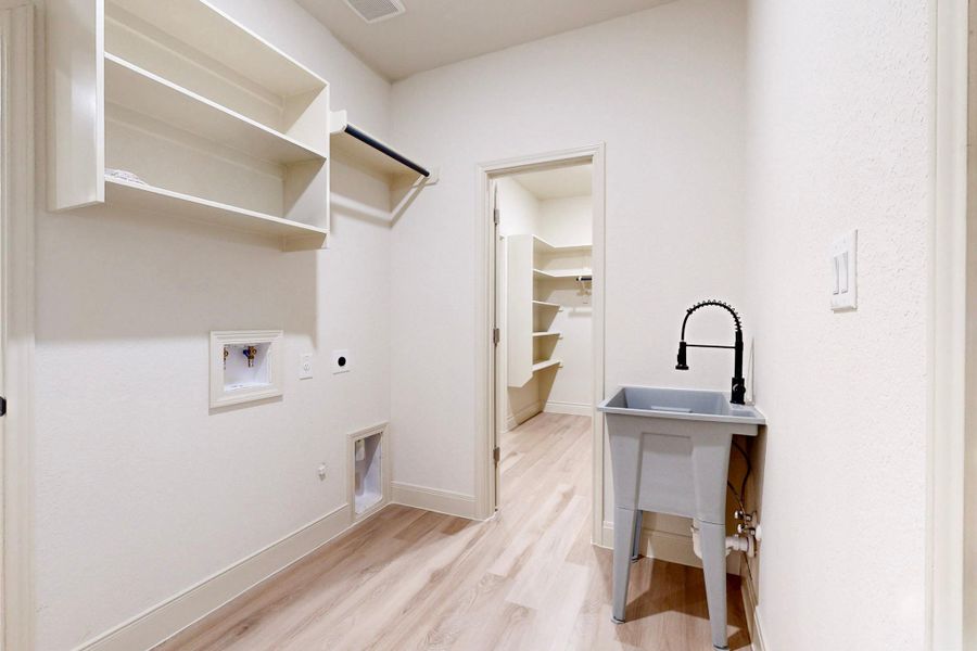 Laundry room featuring wood-finish flooring, built-in shelving, a clothes hanging rod, and a utility sink with a black faucet Laundry room featuring wood-finish flooring, built-in shelving, a clothes hanging rod, and a utility sink with a black faucet