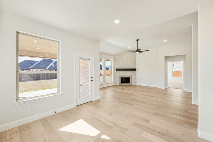 Open living room with light hardwood floors, stone fireplace, ceiling fan, and backyard access door