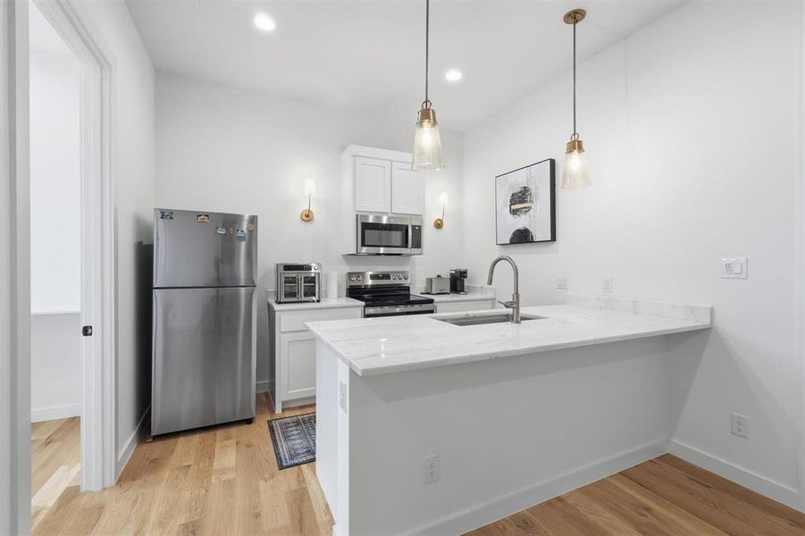 Kitchen with white cabinets, stainless steel appliances, light wood-type flooring, and a peninsula