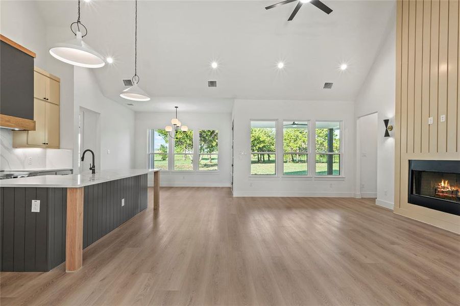 Unfurnished living room featuring high vaulted ceiling, healthy amount of natural light, light wood-style flooring, a large fireplace, and recessed lighting Unfurnished living room featuring high vaulted ceiling, healthy amount of natural light, light wood-style flooring, a large fireplace, and recessed lighting