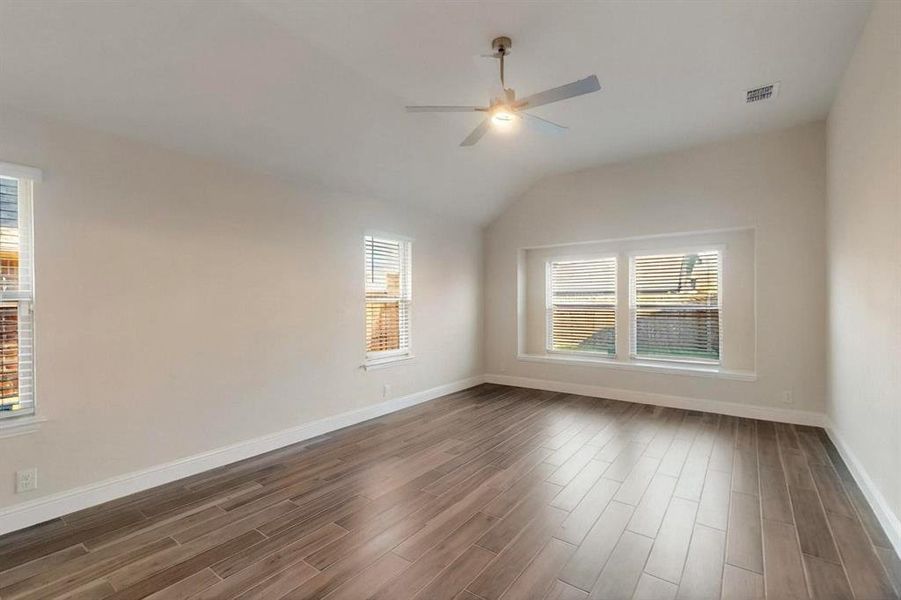 Primary  room with healthy amount of natural light, a ceiling fan, dark wood-style flooring, lofted ceiling, and baseboards