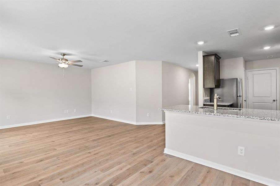 Kitchen with arched walkways, freestanding refrigerator, ceiling fan, light wood-style flooring, and light stone countertops