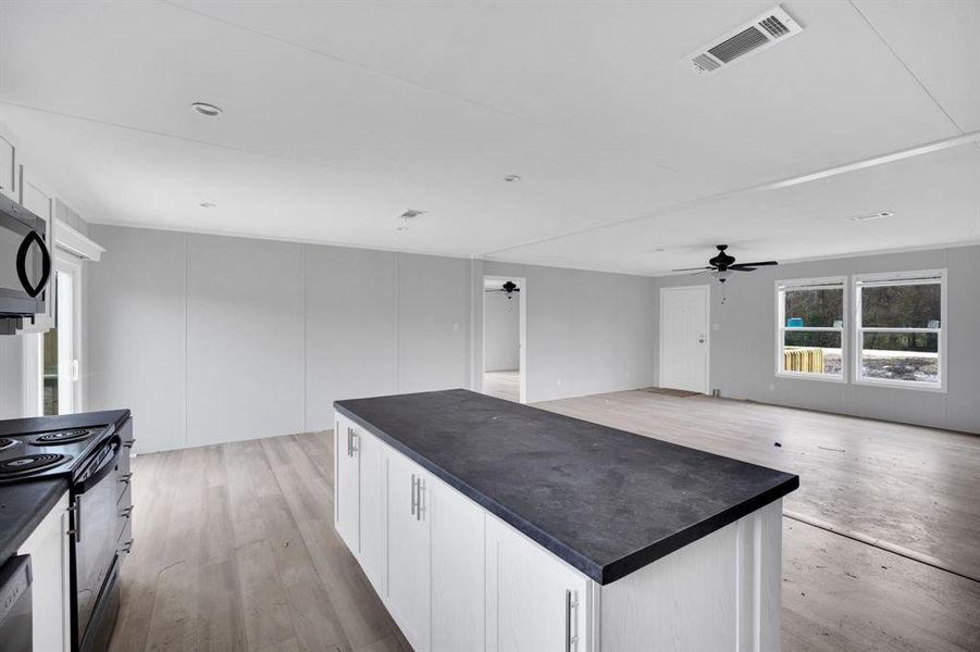 Kitchen featuring white cabinetry, dark countertops, black electric range oven, and a center island