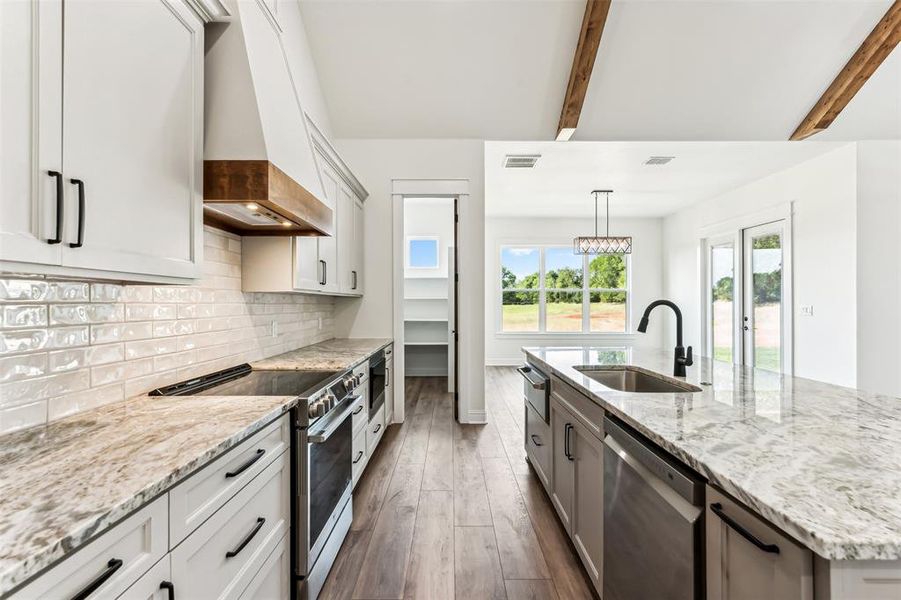 Kitchen featuring stainless steel appliances, built in warming drawer, beamed ceiling, sink, and custom range hood