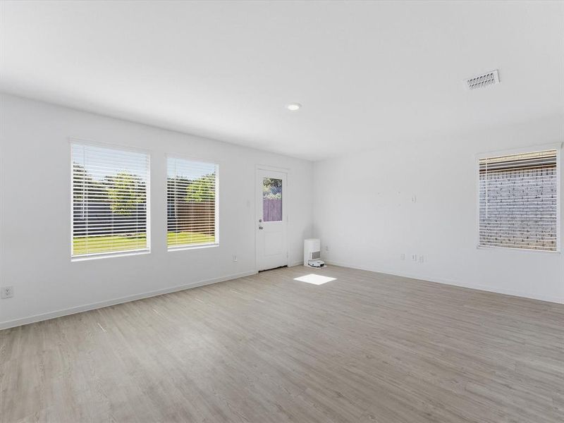 Spacious room featuring wood-finish flooring, multiple windows with blinds, recessed ceiling lighting, and a rear exterior door
